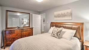 Een slaapkamer met een groot bed, een houten dressoir en een spiegel.