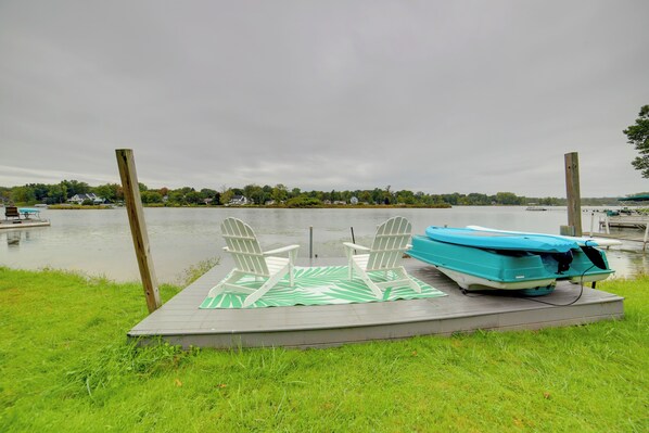 A dock with two Adirondack chairs and a blue boat.