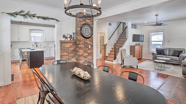 A spacious living area with a large dining table, a fireplace, and a staircase leading to an upper level. - Home Near Downtown & Spearfish Canyon! (Spearfish)