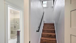 A narrow staircase with wooden steps and a handrail, leading to a room with a glass shower and a white tiled floor. - Home Near Downtown & Spearfish Canyon! (Spearfish)