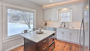 A modern kitchen with white cabinetry, a central island, and a view of a snowy landscape. - Home Near Downtown & Spearfish Canyon! (Spearfish)