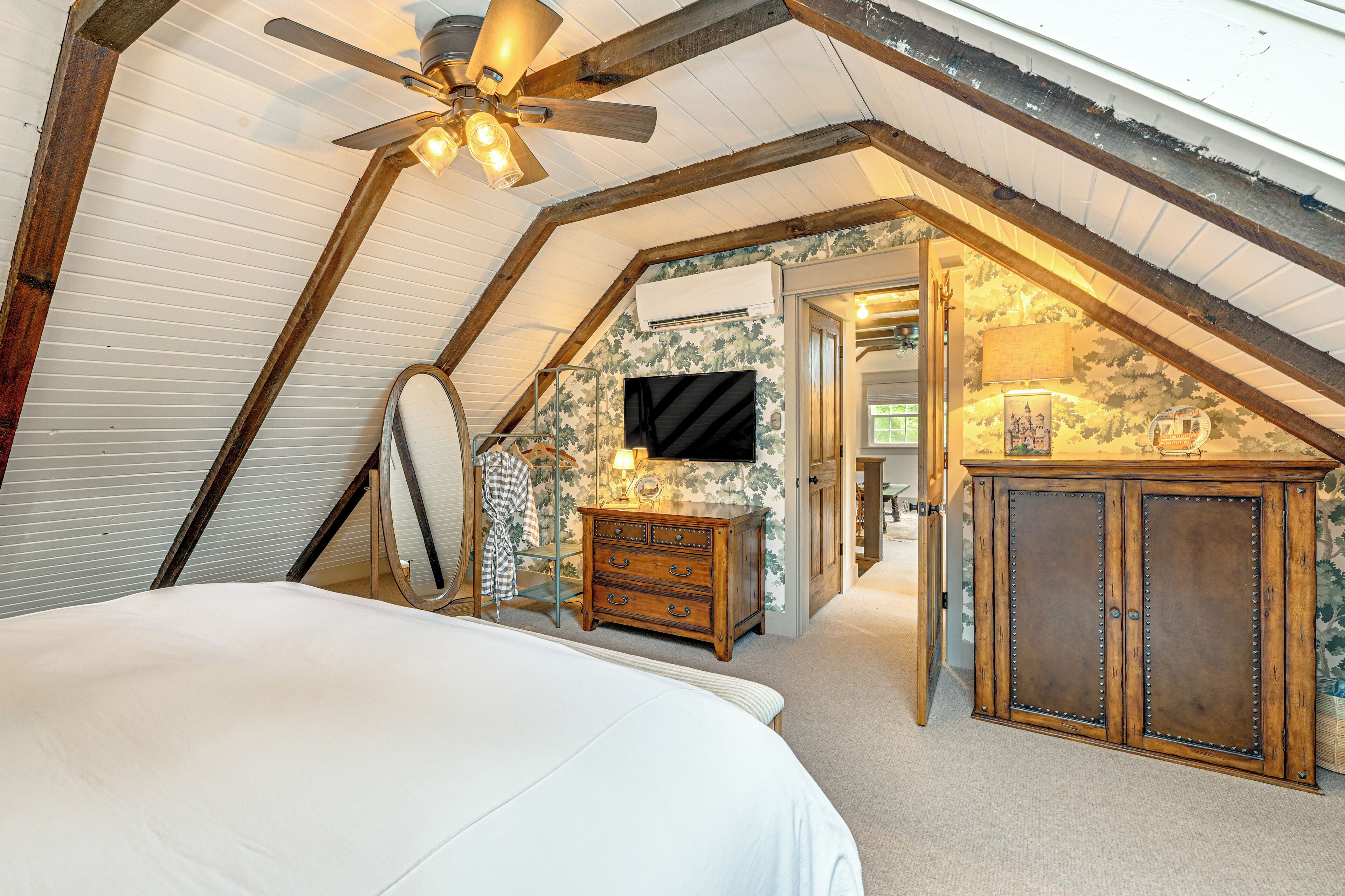 Ein Schlafzimmer mit schrägem Dach, einem Bett, einer Kommode, einem Spiegel und einem Fernseher.