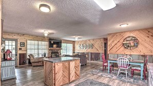A spacious living area with a herringbone-patterned wooden cabinet, a dining table with chairs, and a kitchen area with a built-in oven. - Sues Camp w/ Caddo Lake Access & Dock! (Karnack)