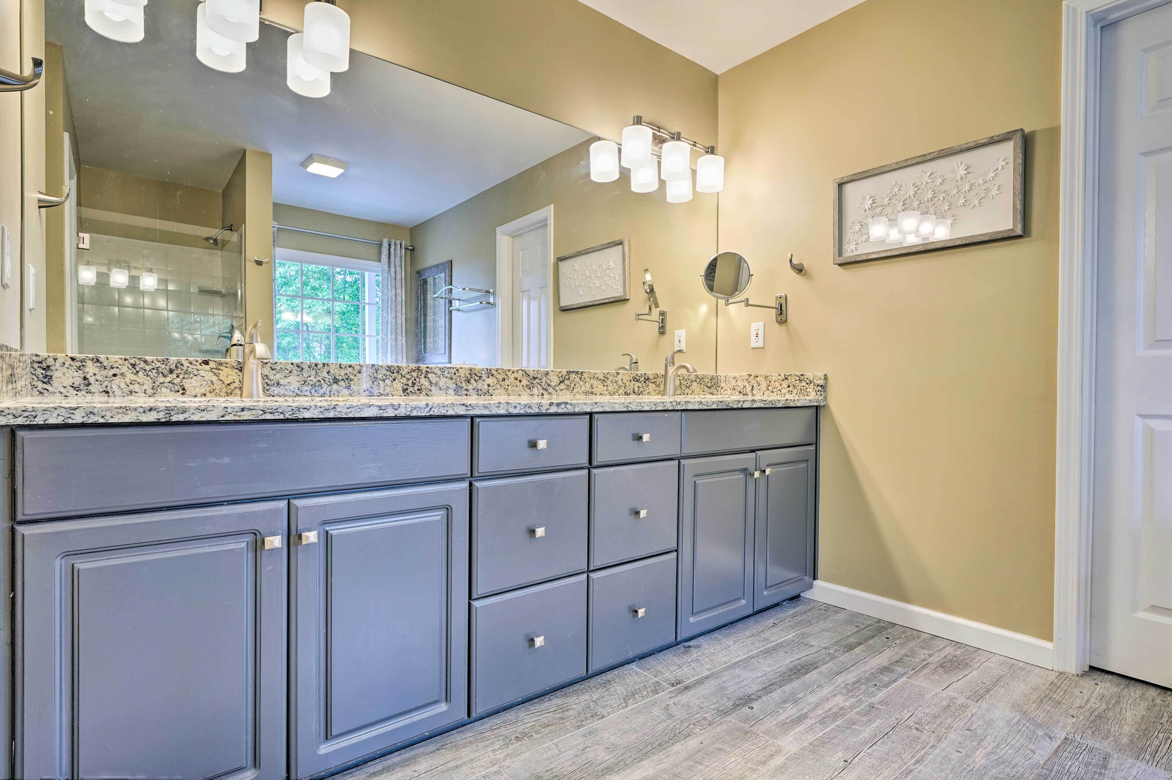 A modern bathroom with a large mirror, granite countertop, and built-in gray cabinets.