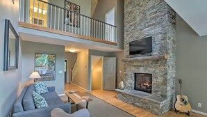 A spacious living room with a stone fireplace, a flat-screen TV, and a guitar.
