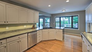 A kitchen with white cabinets, a granite countertop, and a large window with a view of the outdoors.