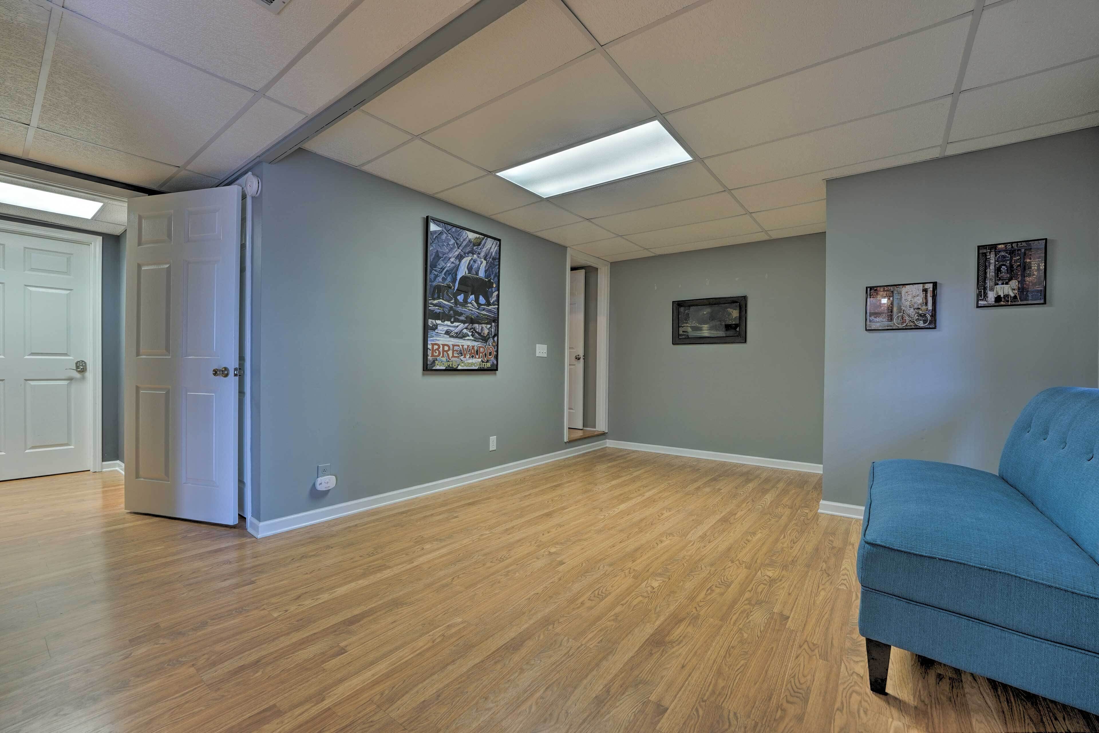 A spacious room with wooden flooring, a blue sofa, and framed pictures on the walls.
