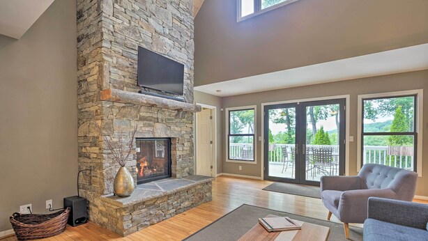 A spacious living room with a stone fireplace, comfortable seating, and large windows offering a view of the outdoors.