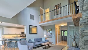 A spacious living area with a high ceiling, a kitchen in the background, a sofa, a coffee table, and a stone accent wall.