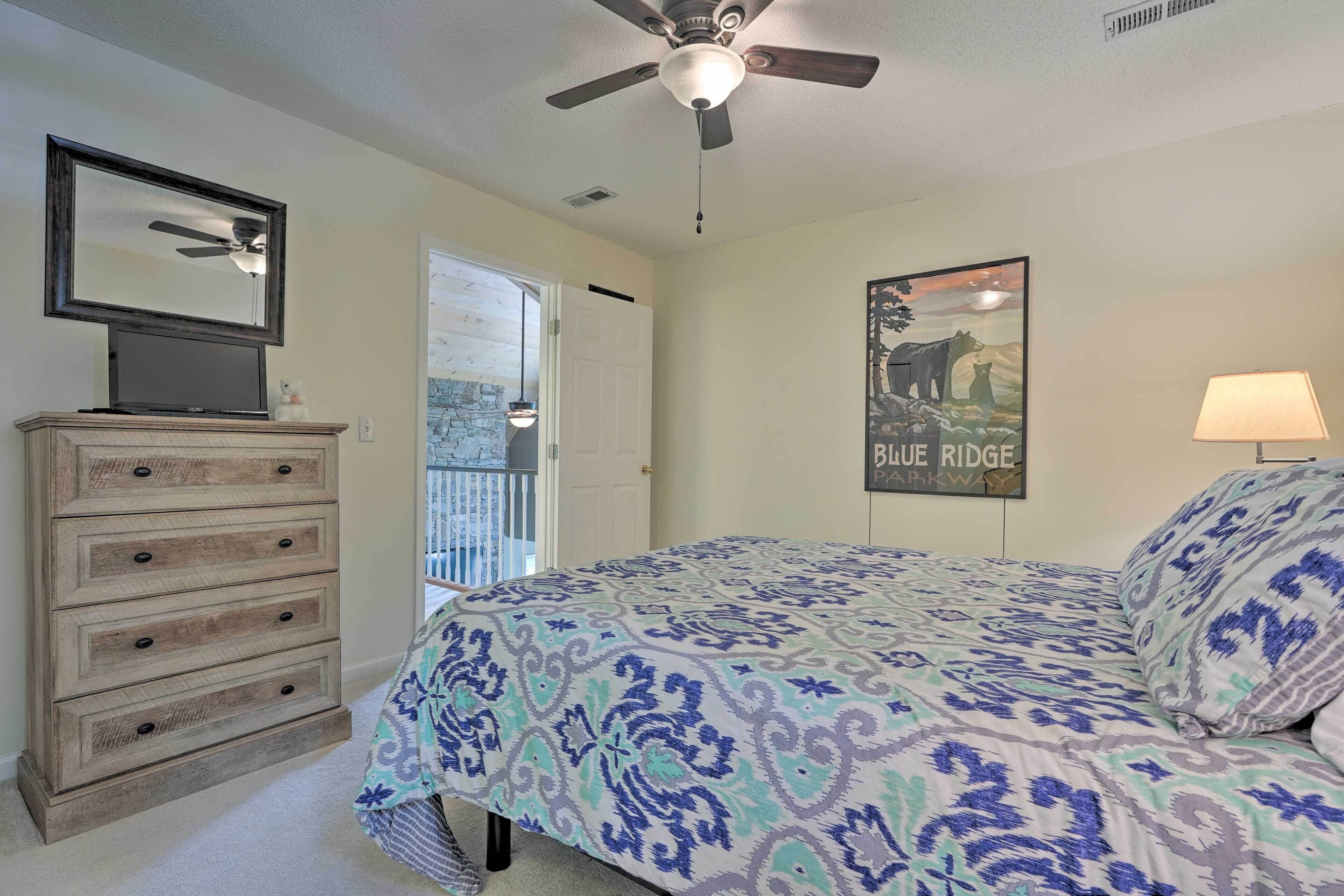 A bedroom with a bed, dresser, ceiling fan, and a poster on the wall.