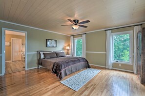 Une chambre à coucher avec un lit, un ventilateur de plafond, de grandes fenêtres et un plancher en bois.