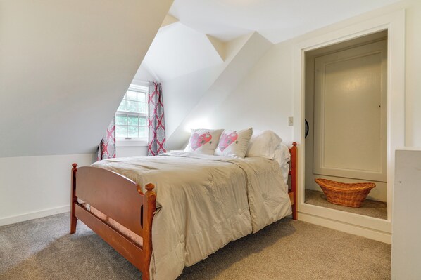 A bedroom with a sloped ceiling, a wooden bed, a window with curtains, and a door leading to another room. - Londonderry Retreat ~ 3 Mi to Lowell Lake! (Londonderry)