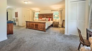 Un dormitorio con una cama de madera grande, dos mesitas de noche, un tocador, una silla, un armario y una ventana con cortinas.