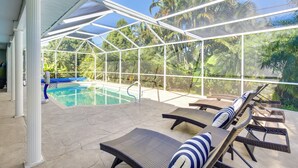 Ein überdachter Poolbereich mit Liegestühlen und Blick auf Palmen.