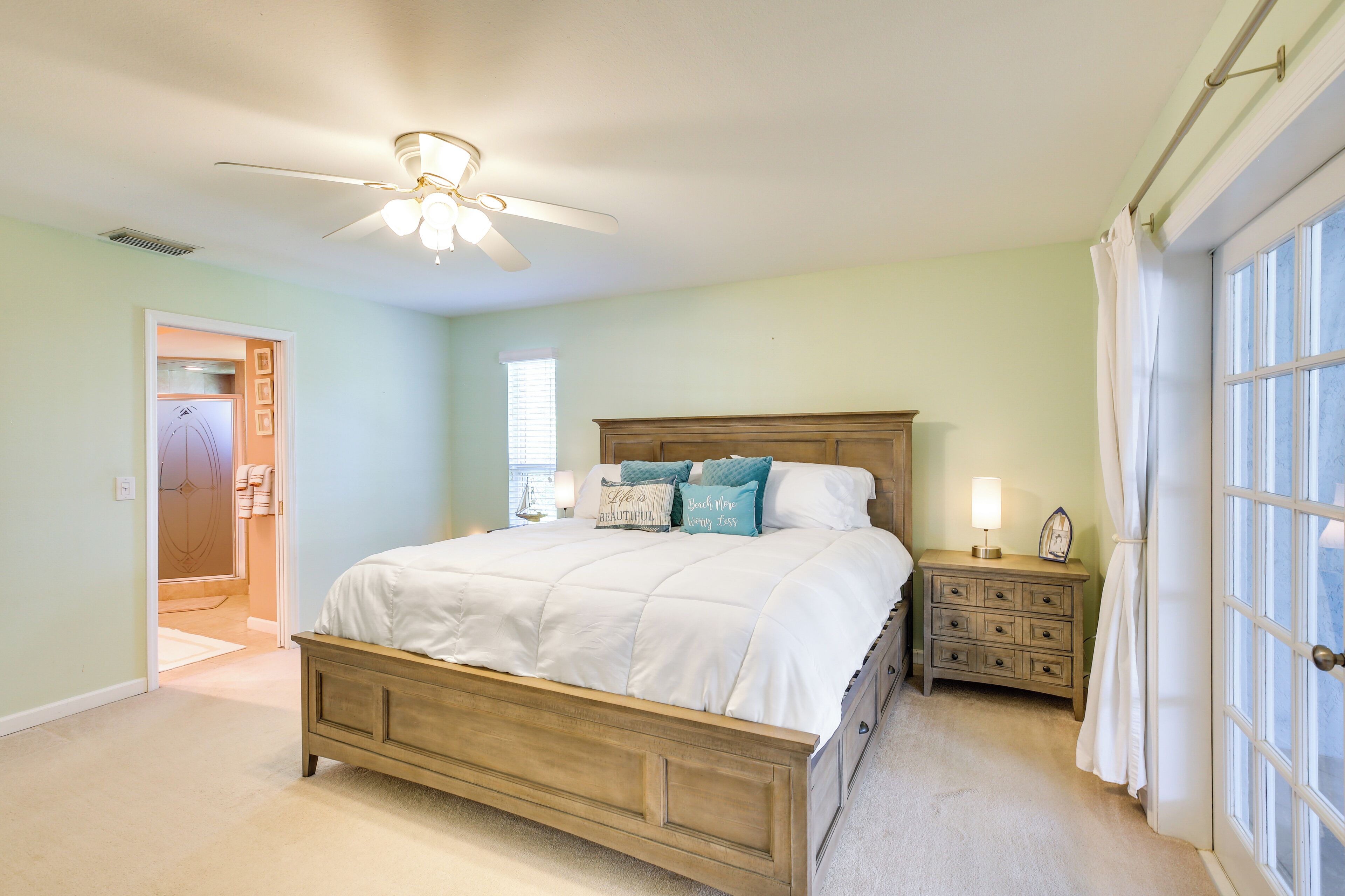 A bedroom with a wooden bed, a nightstand, a ceiling fan, and a window with curtains.