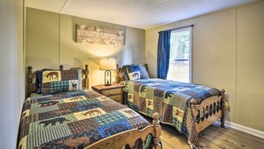 A bedroom with two wooden beds, each with a quilted headboard and a decorative pillow. A nightstand with a lamp is between the beds. - Cozy House w/ Huge Yard ~ 16 Mi to Fort Bragg (Lillington)
