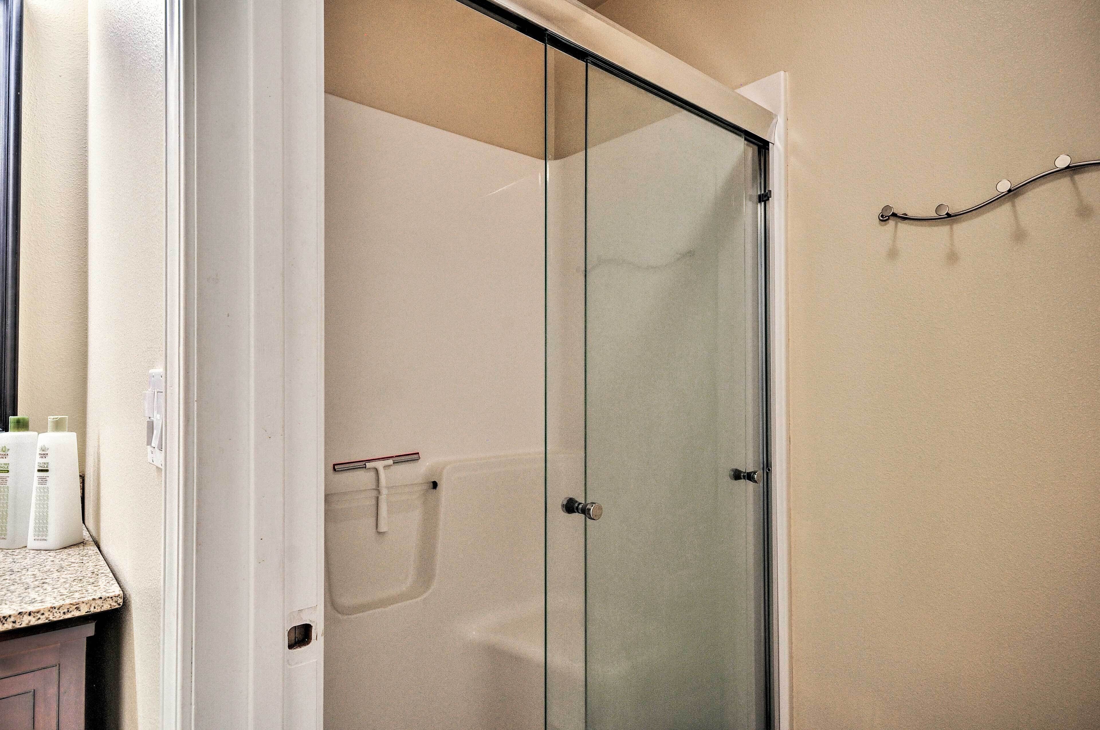 Une douche fermée par des parois en verre, avec une porte blanche, un porte-serviettes fixé au mur et des articles de toilette disposés sur un plan de travail.