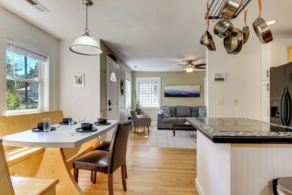 Une cuisine moderne dotée d’un îlot central, d’un coin repas avec une table et des chaises, et d’un salon avec un canapé et un ventilateur de plafond.