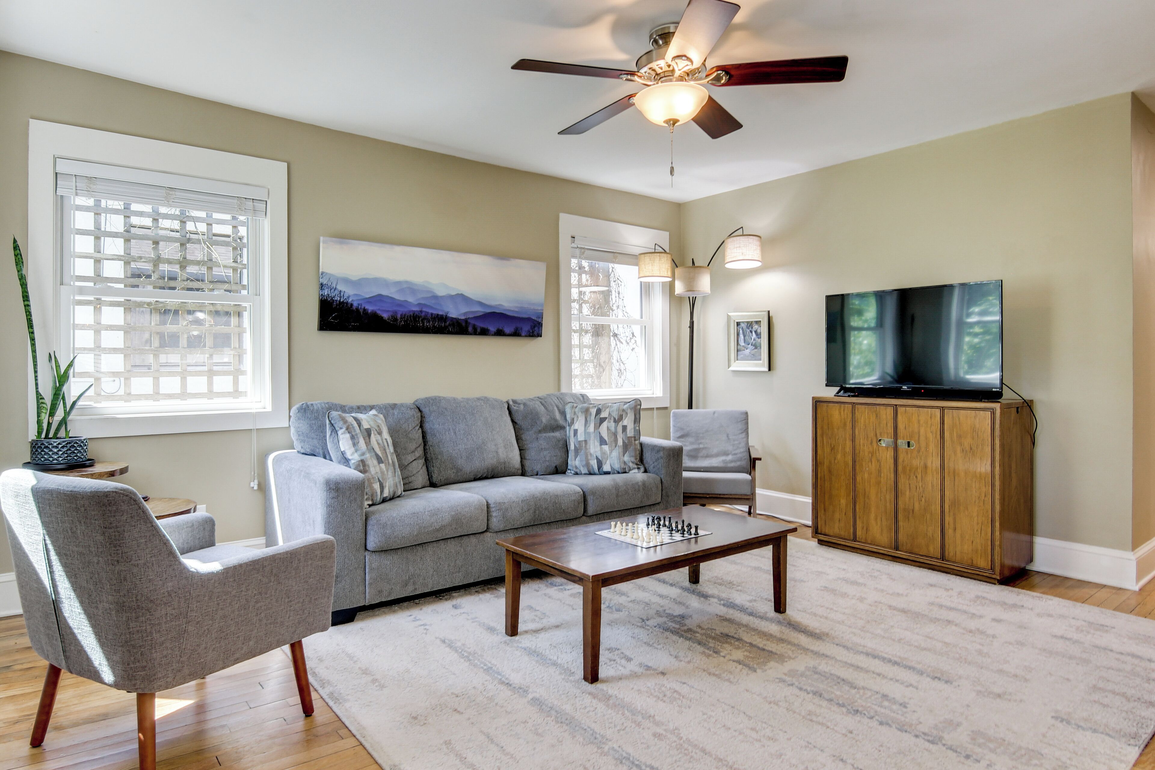 A living room with a grey sofa, a wooden coffee table, a TV on a wooden cabinet, and a ceiling fan.