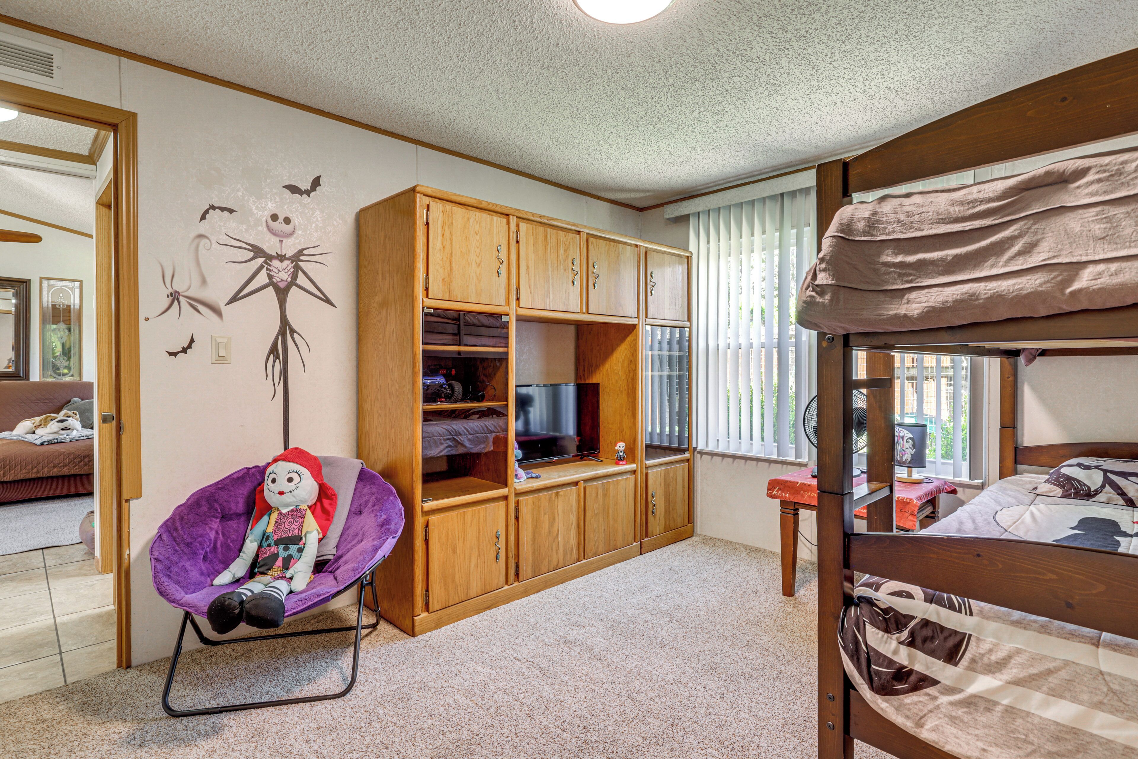 A bedroom with a bunk bed, a wooden wardrobe, a purple chair, and a wall mural.