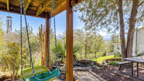 A covered patio with a swing, a picnic table, and a view of a garden and mountains. - Sevierville Home: Lookout Deck, 10 Mi to Dollywood (Sevierville)
