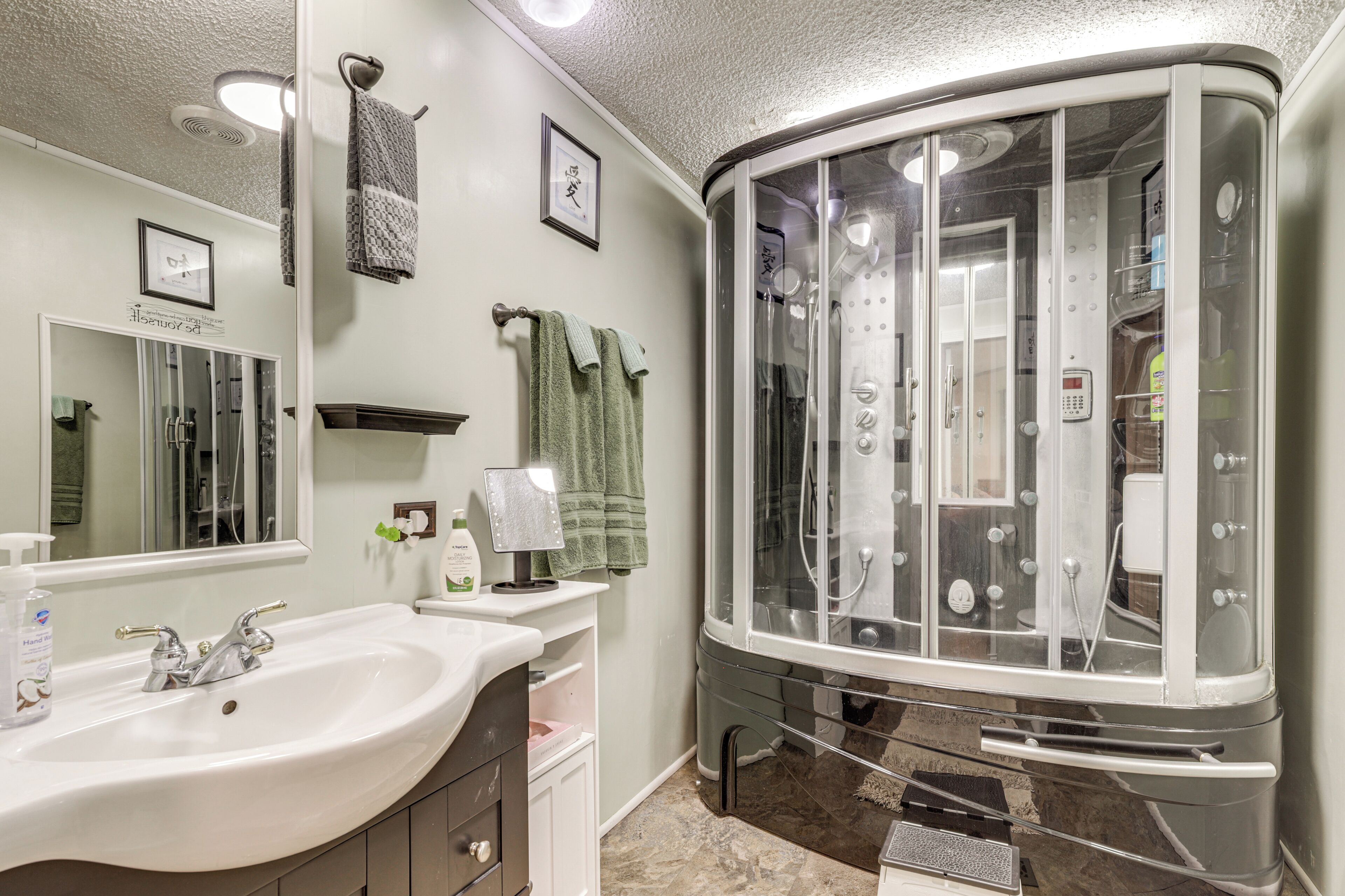 A bathroom with a sink, mirror, towel rack, shower enclosure, and a vanity.