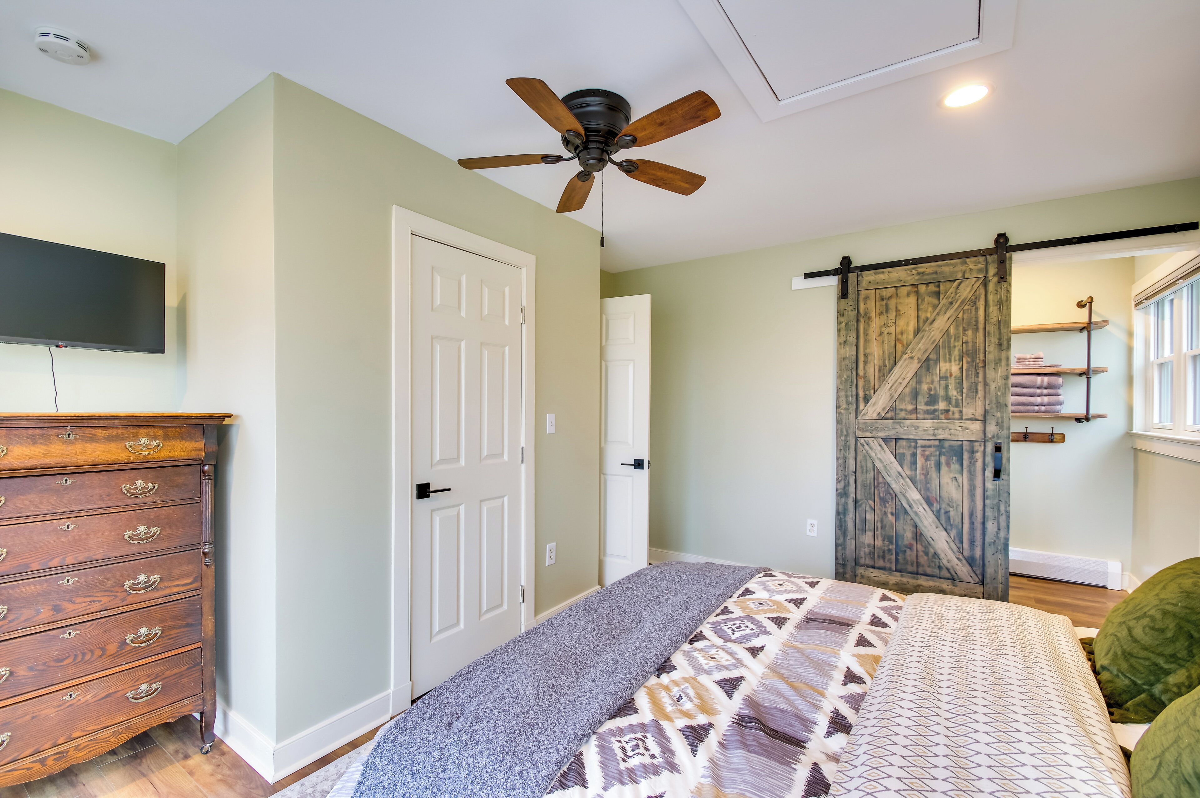 A bedroom with a bed, a dresser, a ceiling fan, a sliding barn-style door, and a mounted TV.