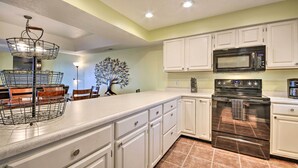 Una cocina con gabinetes blancos, horno de acero inoxidable, microondas e iluminación.
