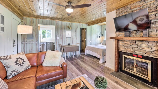 L’intérieur d’un chalet accueillant, avec un plafond en bois, une cheminée, un téléviseur fixé au-dessus, un coin repas avec une table et des chaises, et un lit à l’arrière-plan.