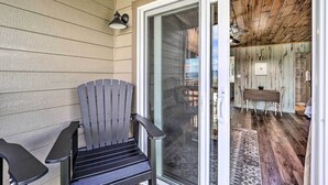 Un mur extérieur en bois, une porte-fenêtre coulissante, un fauteuil Adirondack noir et un coin repas avec une table et des chaises à l’intérieur.