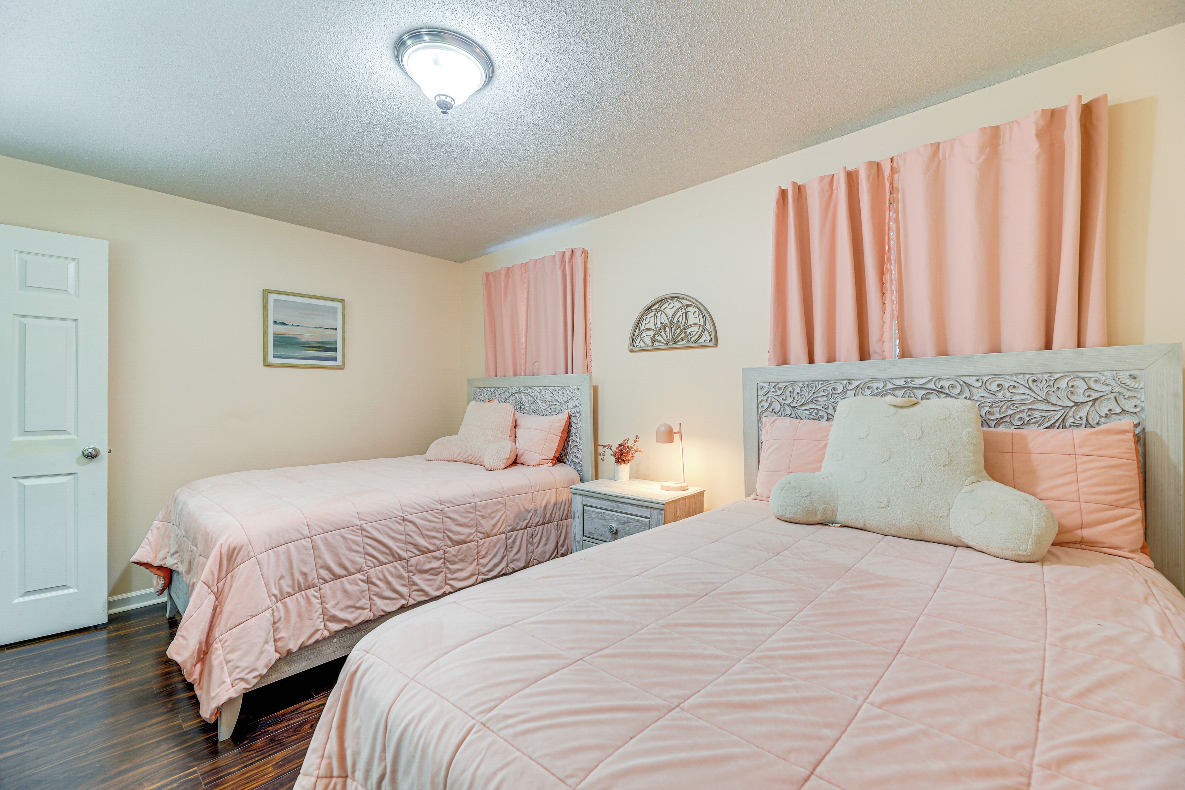A bedroom with two beds, a nightstand, a lamp, and a door.