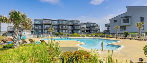 A modern hotel with a pool area, multiple balconies, and a clear blue sky.
