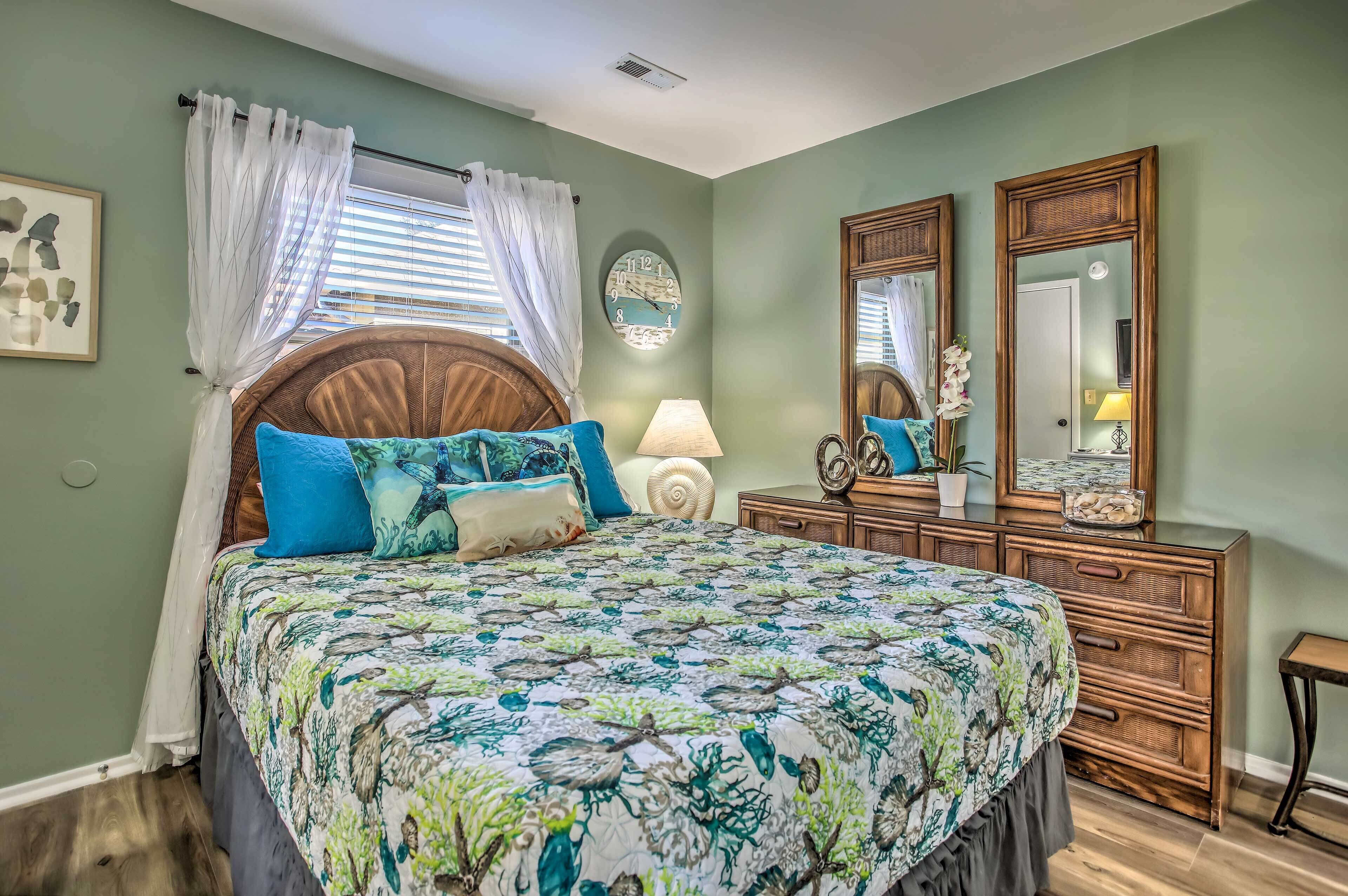 A bedroom with a large bed, a wooden dresser, a mirror, and a wall clock.