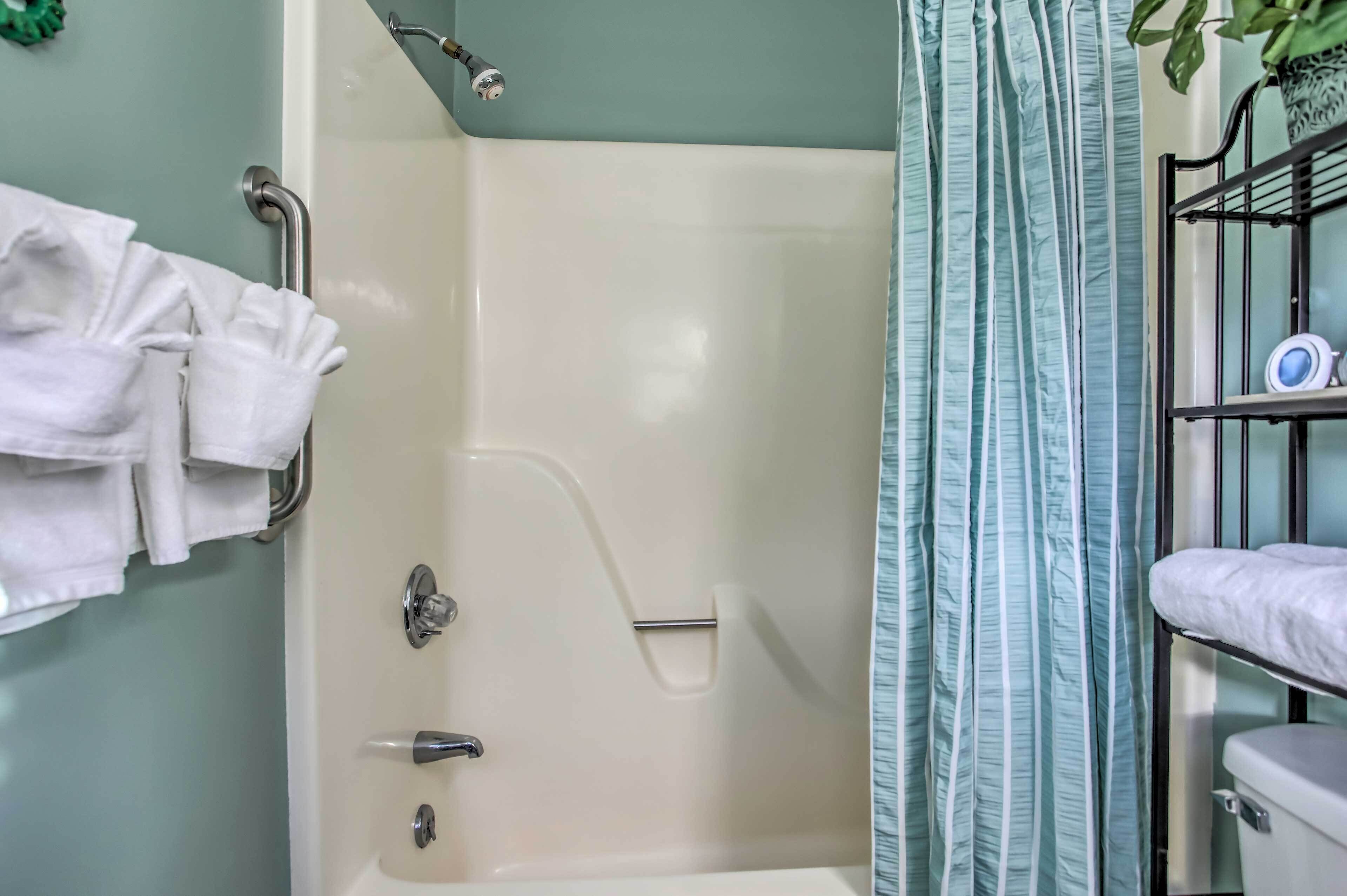Une salle de bain avec une baignoire, une douche et des toilettes. On y trouve un porte-serviettes avec des serviettes, une étagère avec des articles de toilette et une plante en pot.
