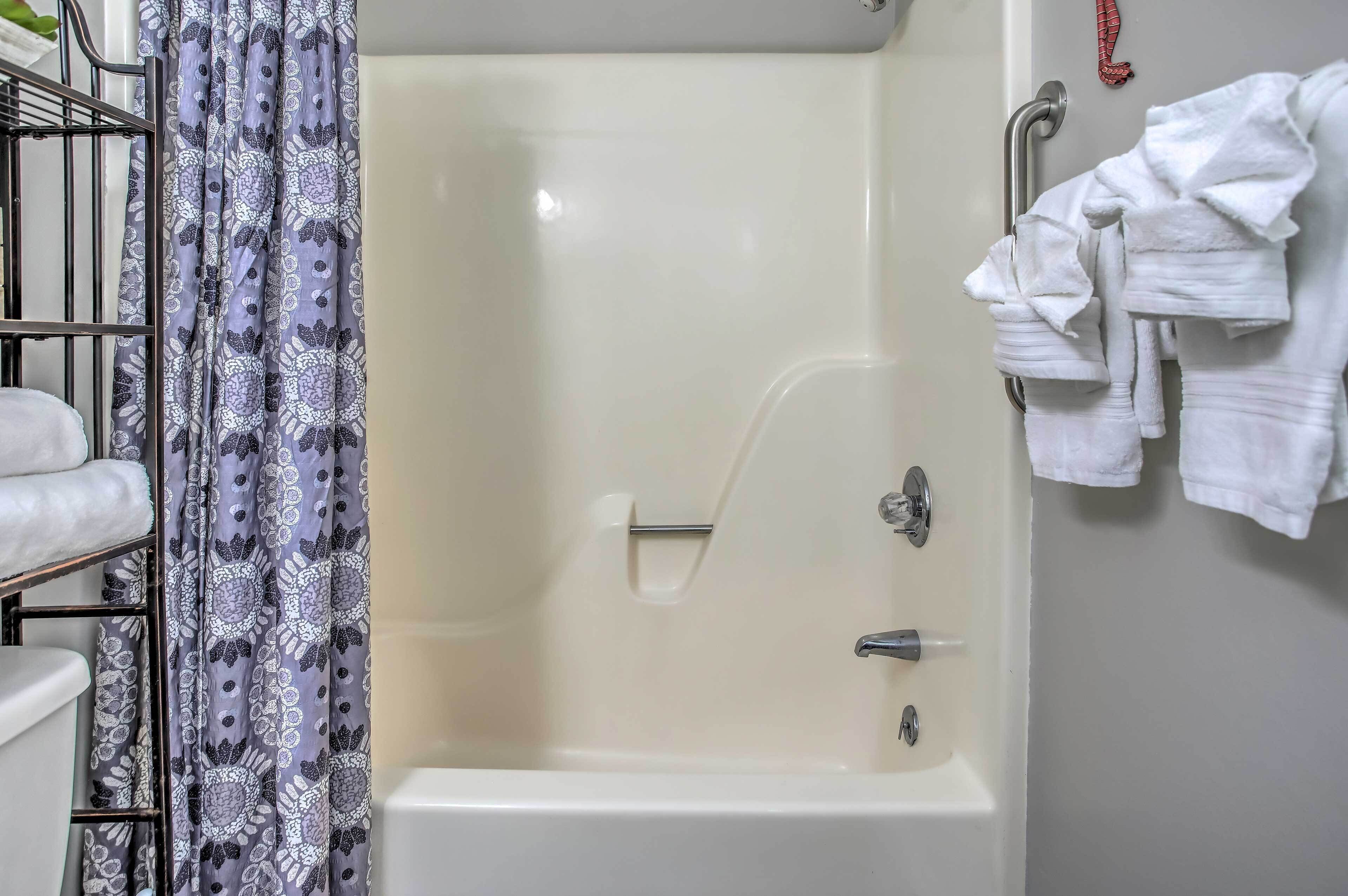 A bathtub with a shower curtain, a towel rack with white towels, and a metal shelf with folded towels.