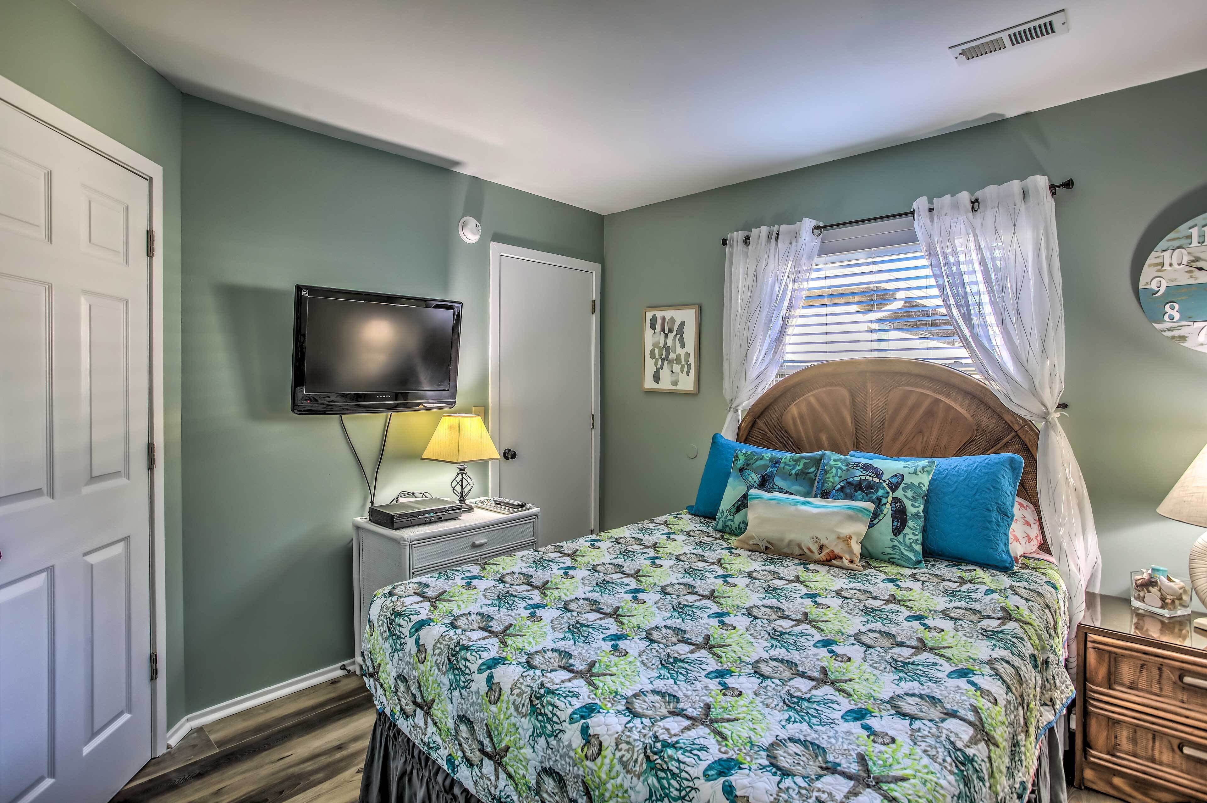 A bedroom with a bed, a television, a bedside table with a lamp, a window with curtains, and a wall clock.