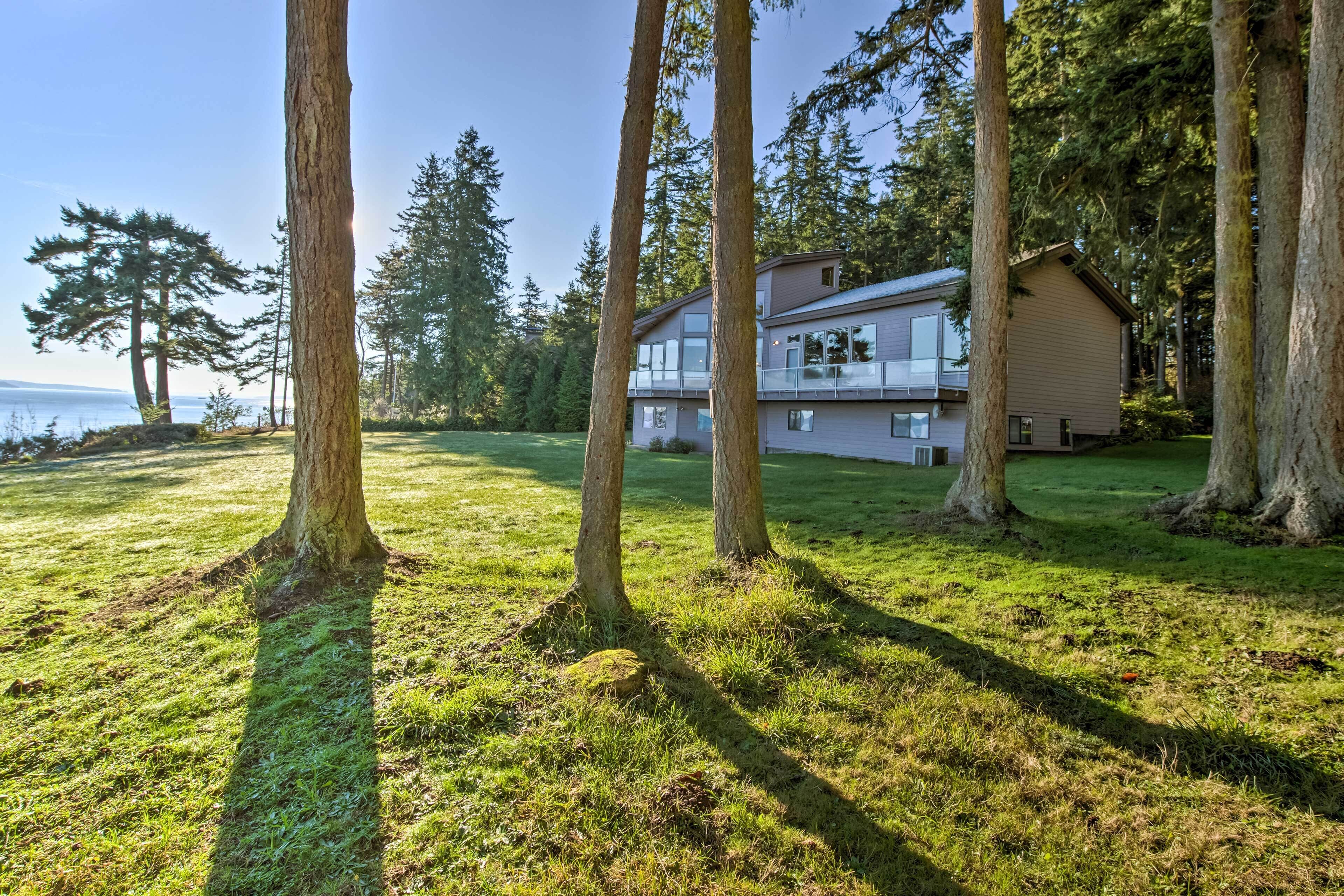 A two-story house with a balcony, surrounded by tall trees and a grassy lawn.