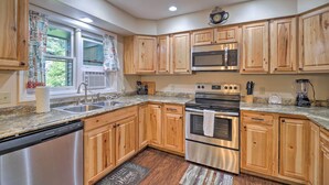 A kitchen with wooden cabinets, stainless steel appliances, a dishwasher, and a window with curtains. - Lake Placid Home ~ 9 Mi to Whiteface Mtn! (Lake Placid)