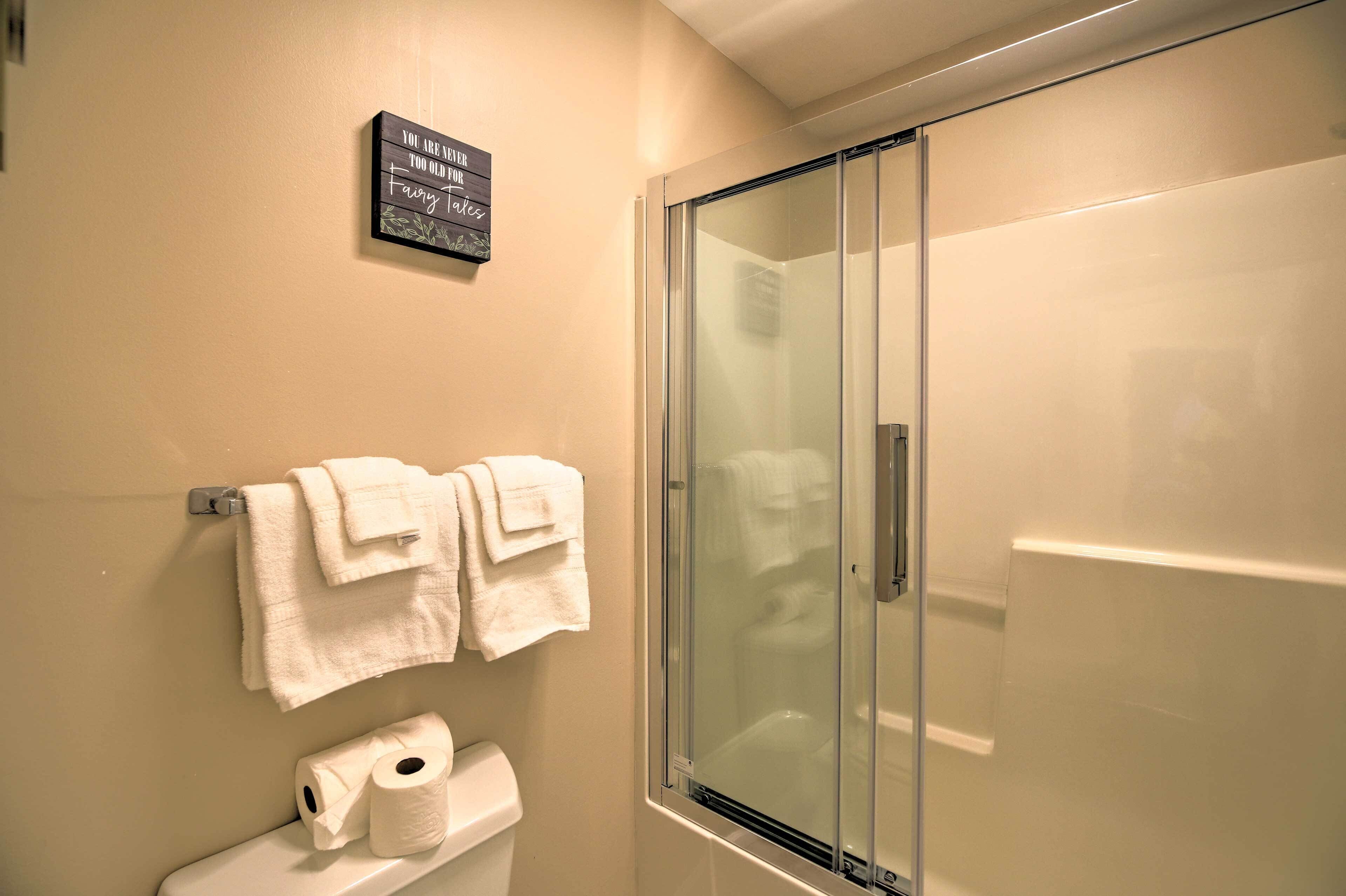 Een badkamer met een douchecabine van glas, een toilet met toiletpapier, en twee handdoeken aan een rek.