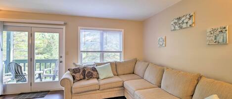 A living room with a beige sectional sofa, a glass door leading to an outdoor deck, and two wall-mounted artworks.