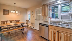 A kitchen with wooden cabinets, a built-in dishwasher, a double sink, and a dining area with a wooden table and benches. - Lake Placid Home ~ 9 Mi to Whiteface Mtn! (Lake Placid)