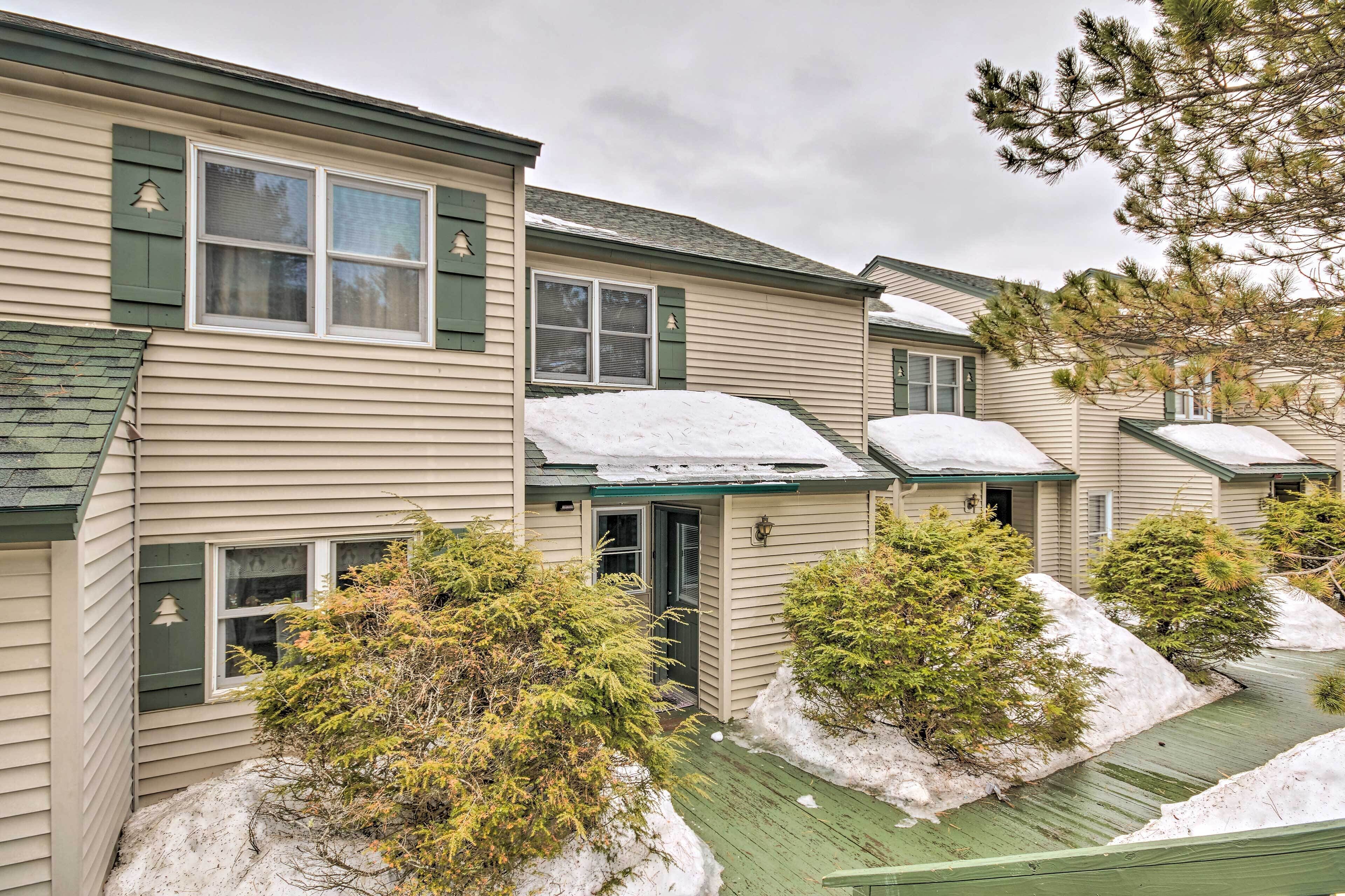 A row of beige houses with green shutters and snow on the roofs.