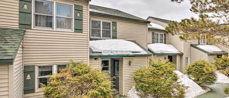 A row of beige houses with green shutters and snow on the roofs.