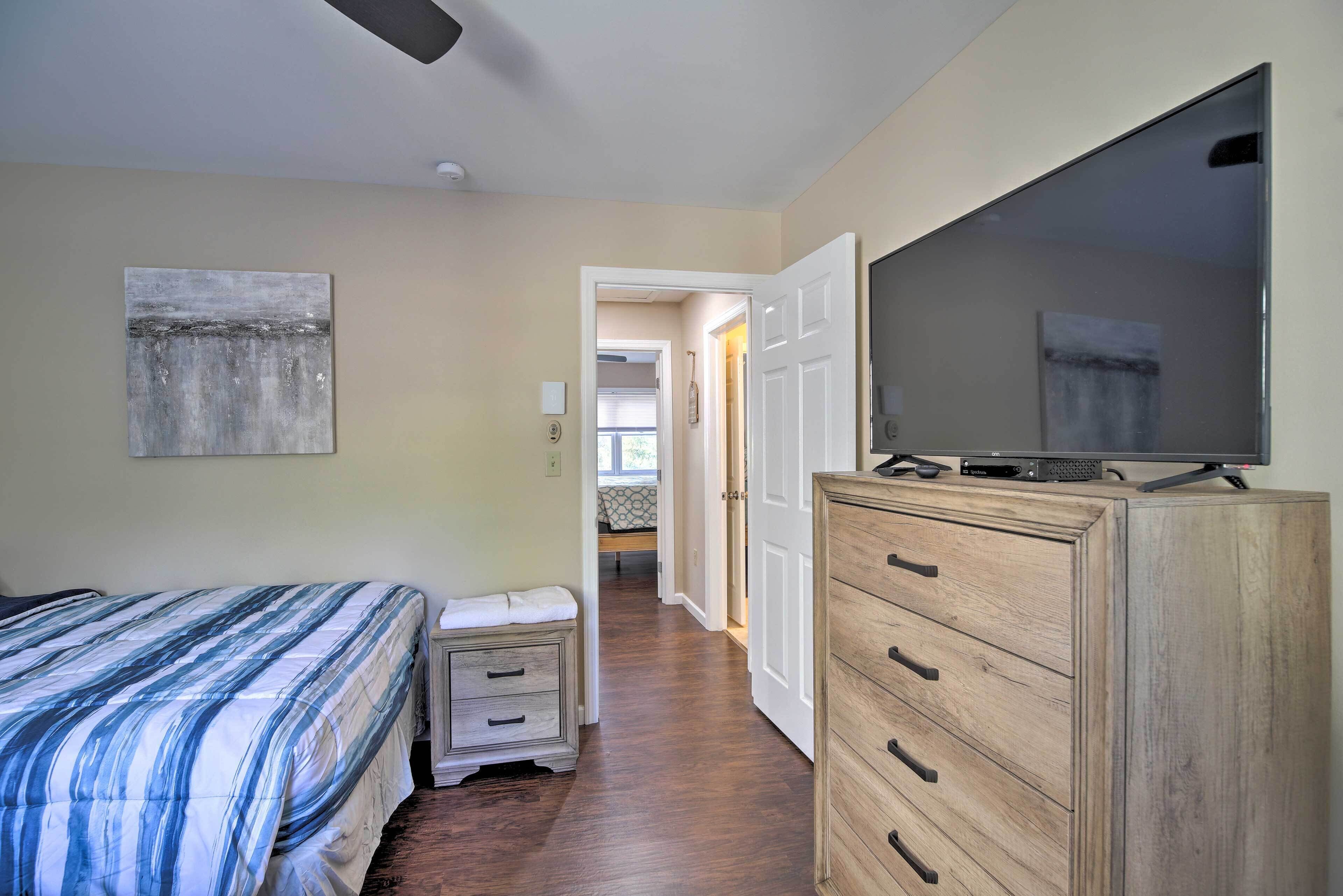 A bedroom with a bed, a TV, a wooden dresser, and a hallway leading to another room.