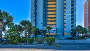 A multi-story hotel with balconies, a parking lot, and palm trees. - Myrtle Beachfront Bliss: Pools, Views & Skywheel! (Myrtle Beach)