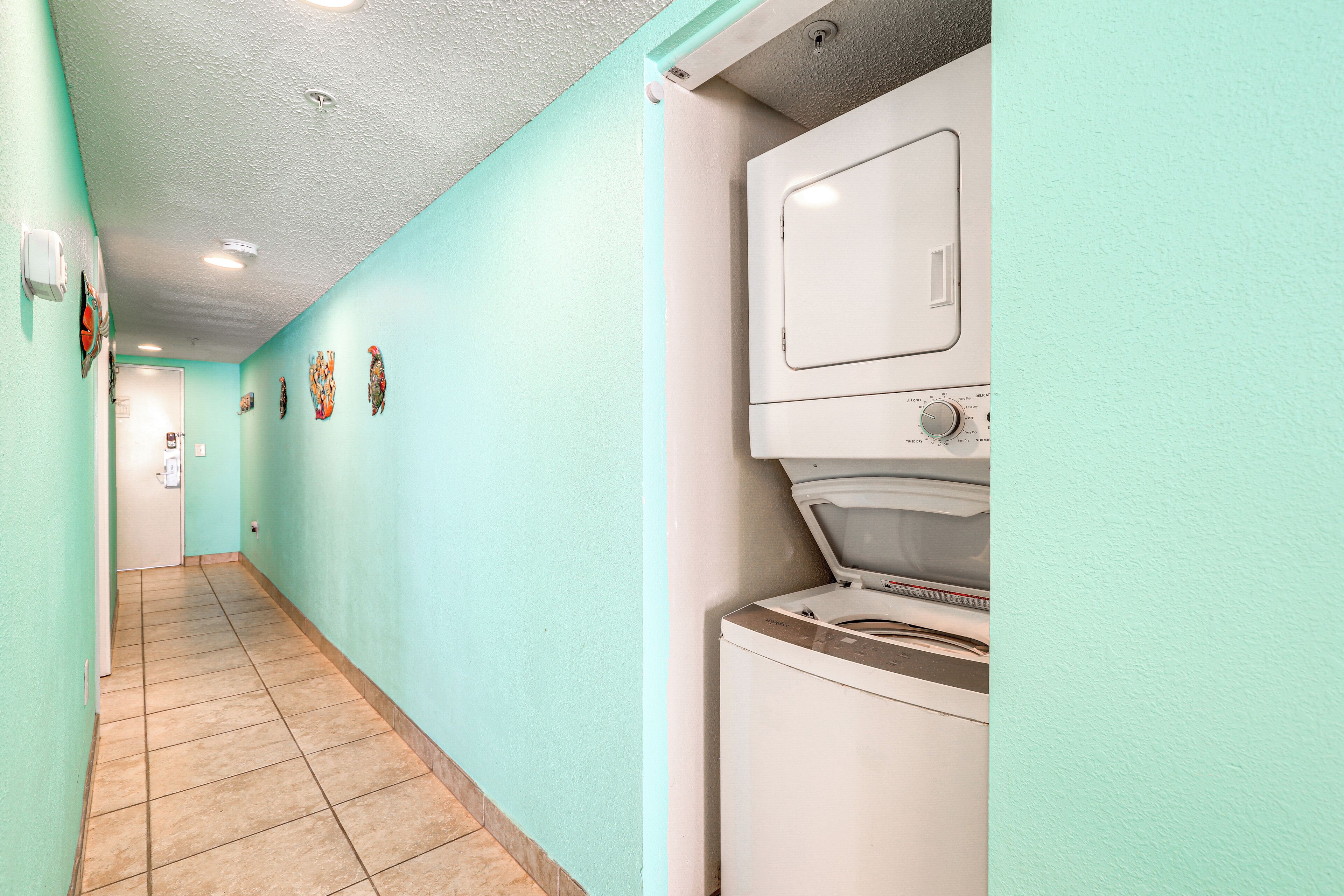 A laundry room with a washing machine and dryer, a tiled floor, and a door at the end of the hallway.