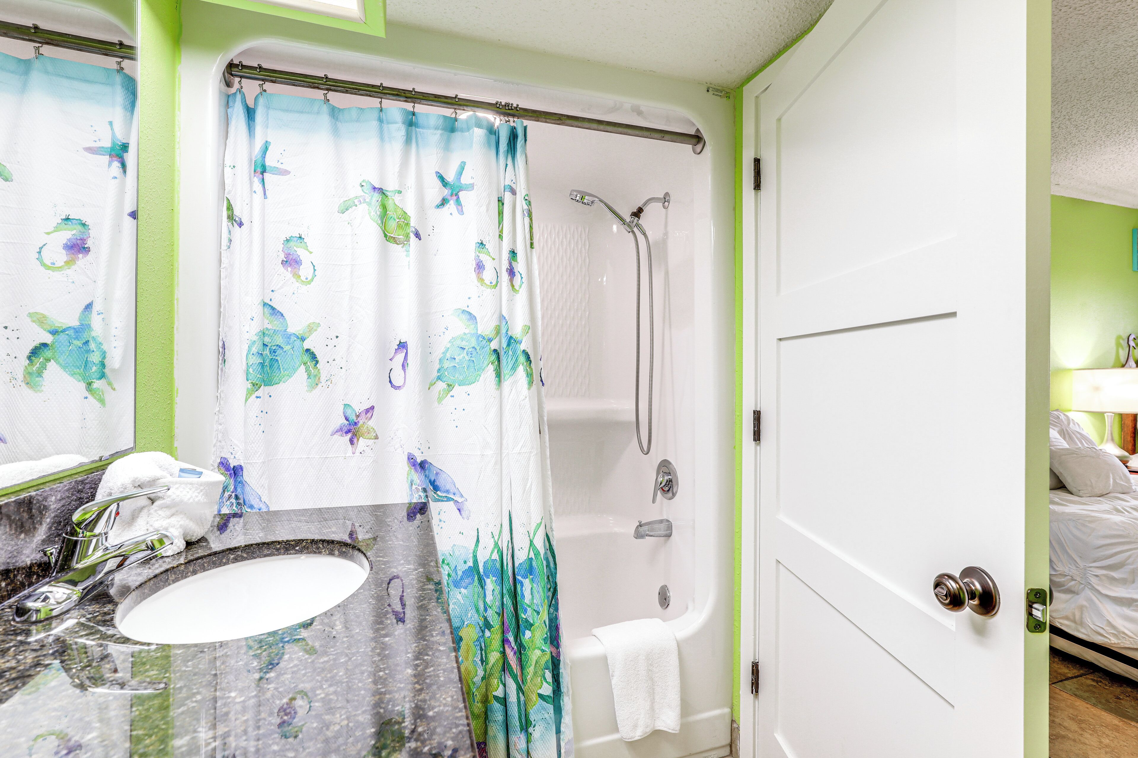 A bathroom with a shower, a sink, and a door leading to a bedroom.