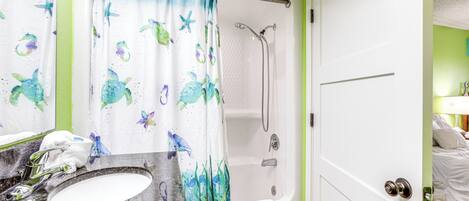 A bathroom with a shower, a sink, and a door leading to a bedroom.