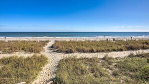 A sandy beach with a clear blue sky and a path leading to the water. - Myrtle Beachfront Bliss: Pools, Views & Skywheel! (Myrtle Beach)