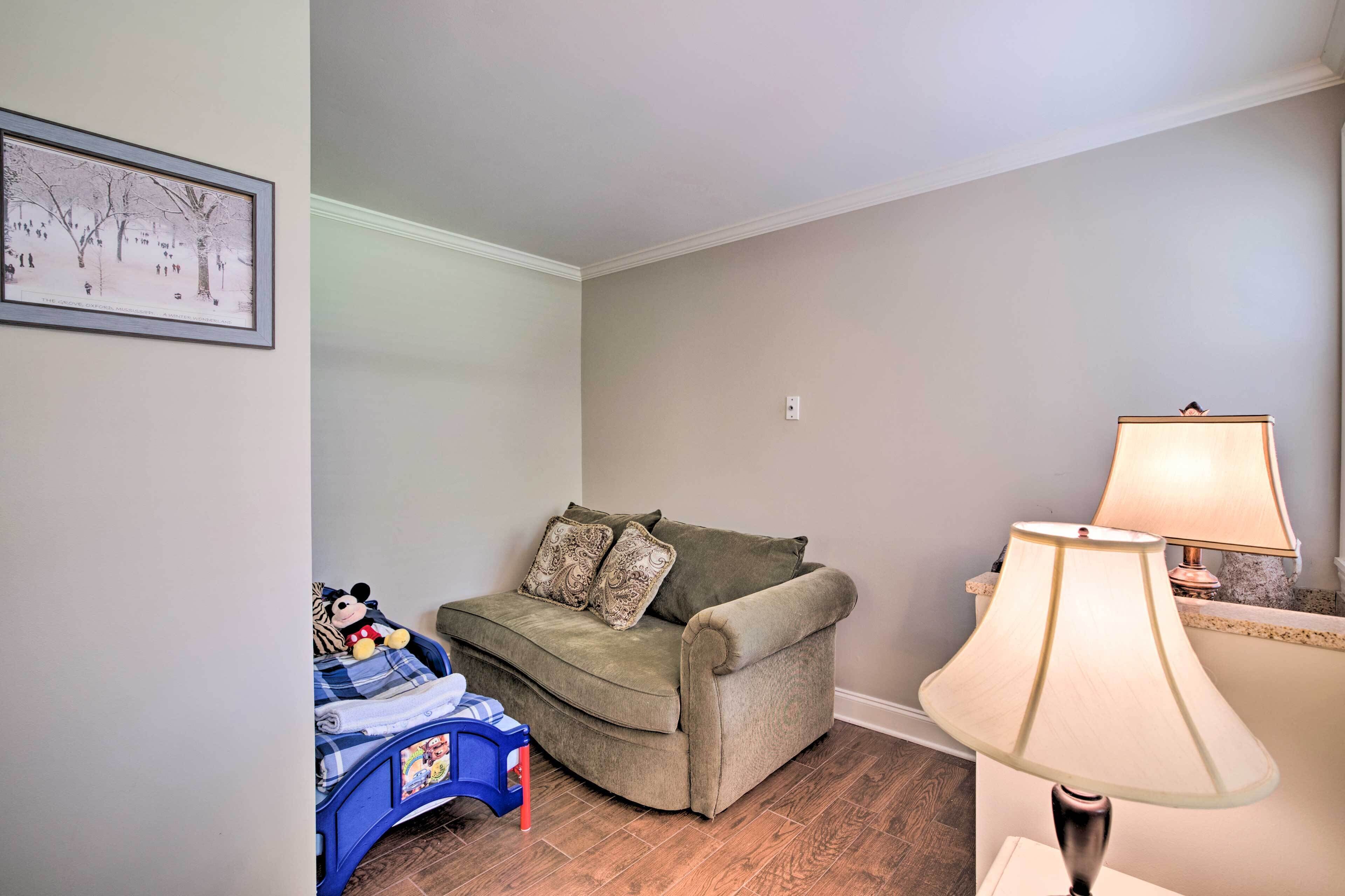 A cozy room with a green sofa, a small blue chair, a lamp, and a framed picture on the wall.